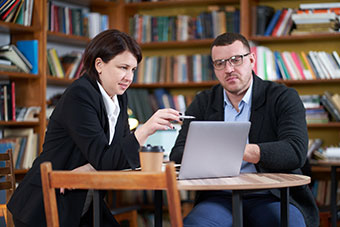 Man and woman working with laptop sitting in modern stylish room with bookshelves on background in library
