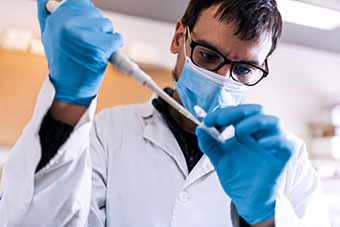 Science researcher wearing face mask filling test tubes in his laboratory.