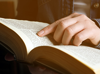 Person reading Holy Bible on blurred background