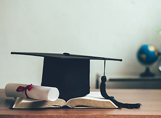 	A mortarboard and graduation scroll on open books on the desk. Education learning concept