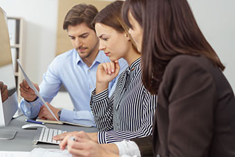 Three people analysing a written report, reading the document with serious expressions