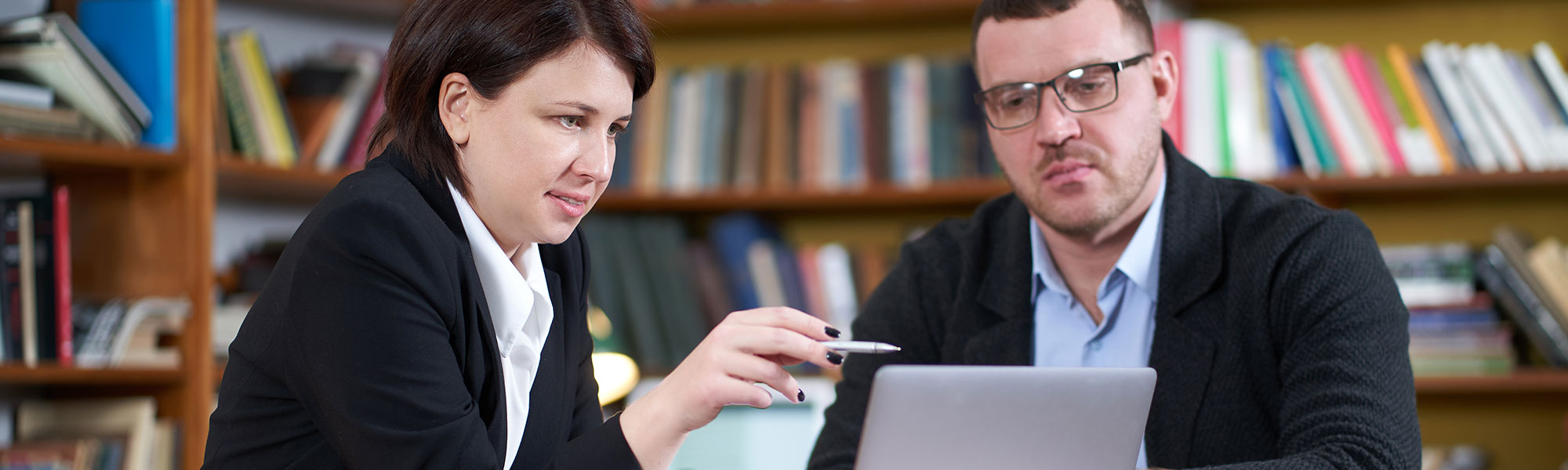 Man and woman working with laptop sitting in modern stylish room with bookshelves on background in library