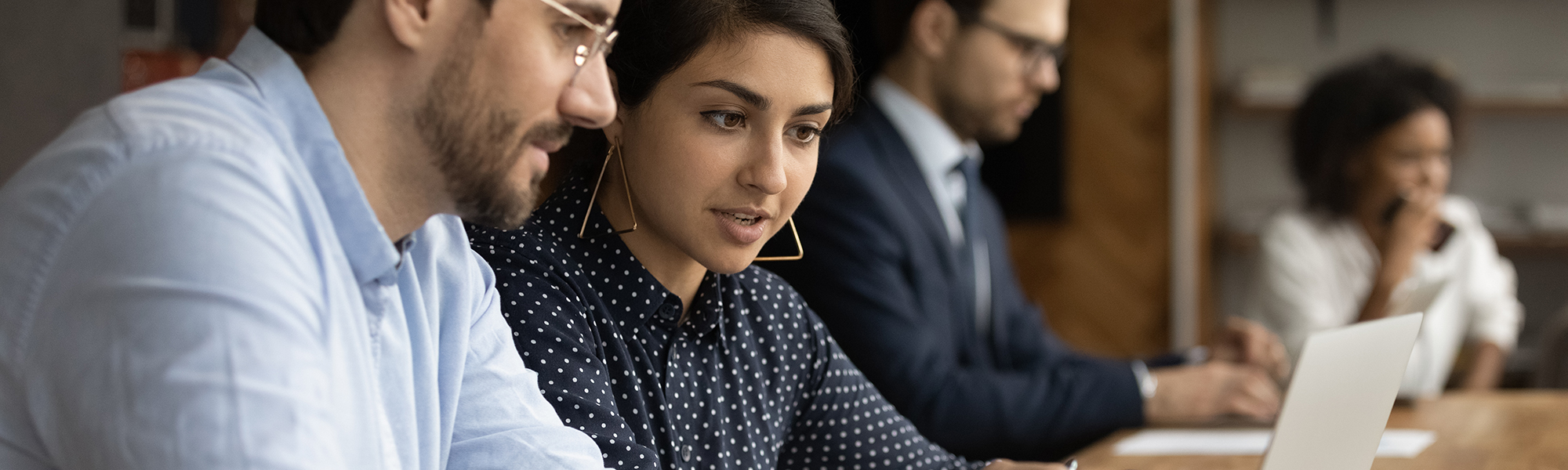 Male looking at laptop and listening to skilled indian female. Hindu woman experienced worker consult young man new employee help in computer work at corporate network.programme_banner