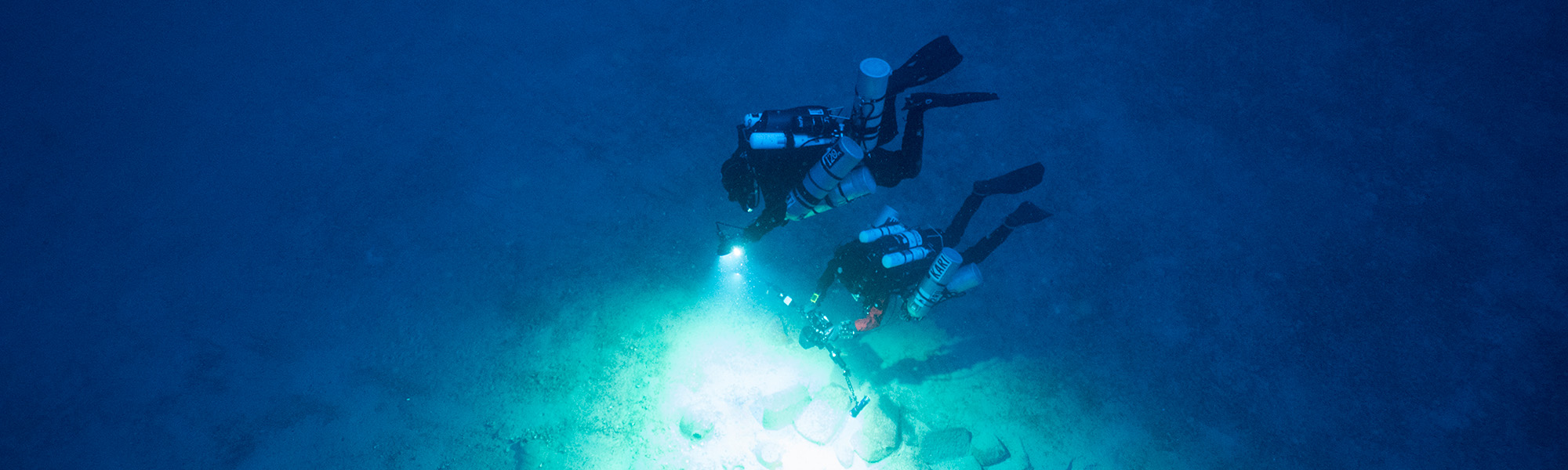 Two divers illuminating underwater pottery