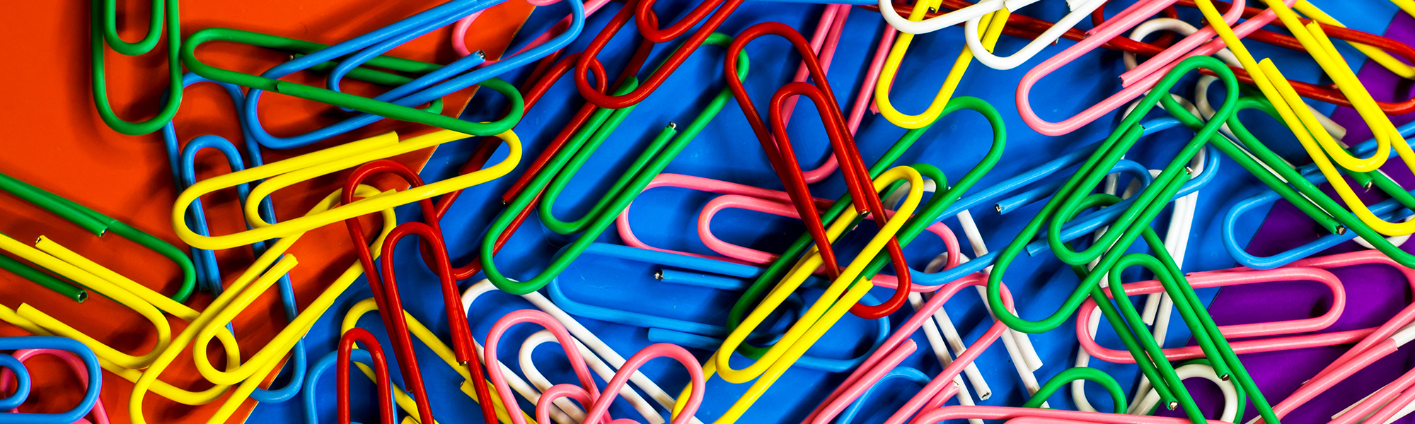Stationery paper clips of different colors group lie on the background of different colors