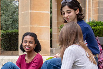 Three students in the open space next to the Dun Karm monument at the UM Msida Campus